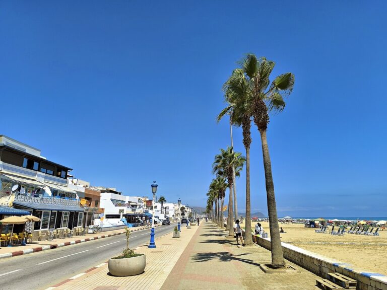 Palm-lined corniche beside Martil Beach, with seafront cafés, sandy shore and the Mediterranean Sea.